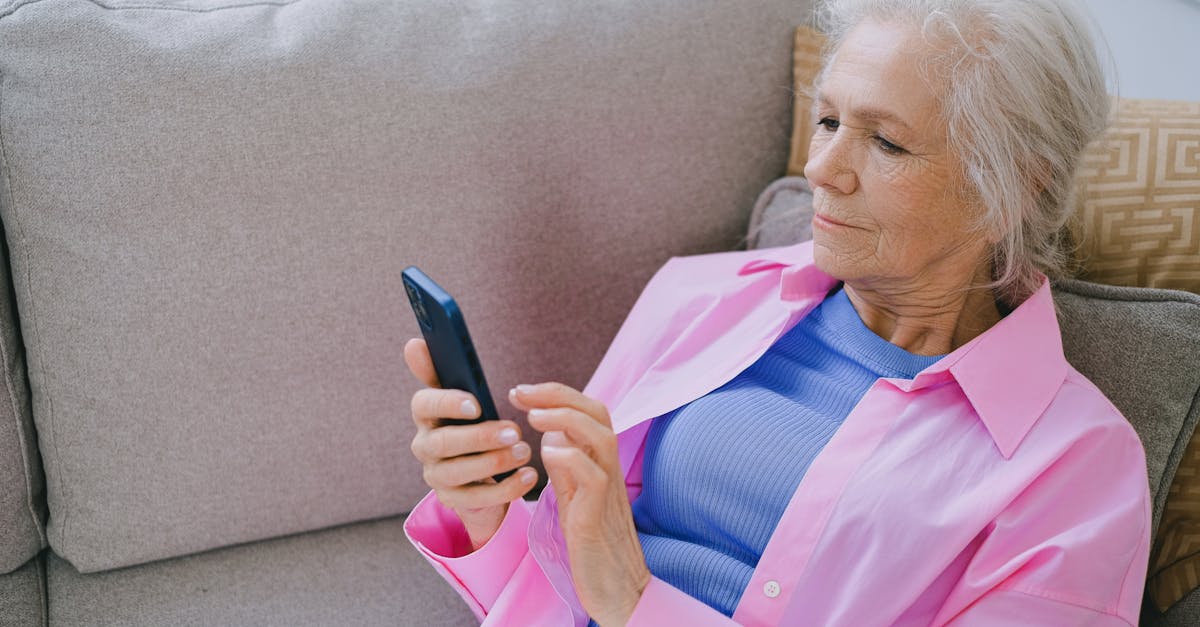 Elderly woman relaxing on sofa while using smartphone for communication.