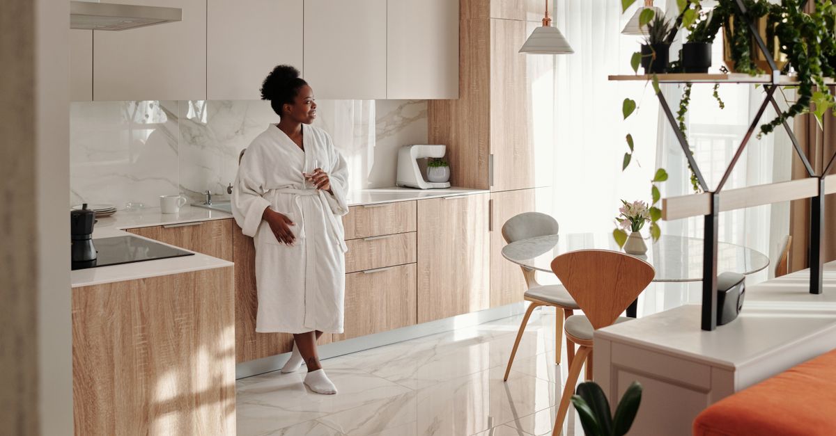 Woman in bathrobe enjoying a peaceful morning in a stylish kitchen with natural light.