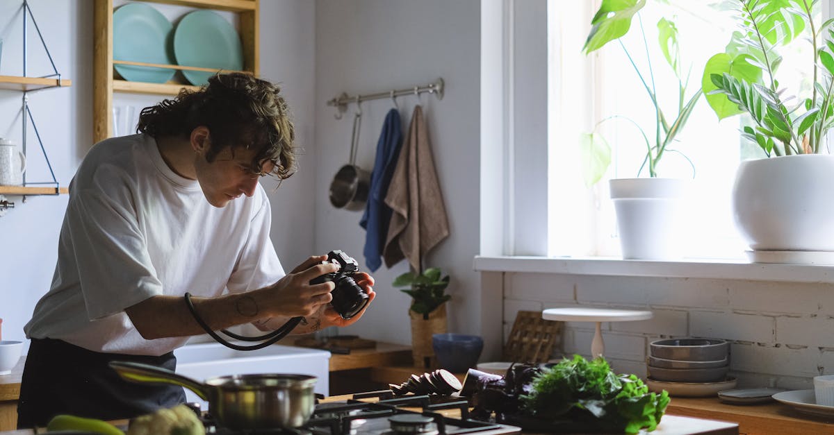 A man photographing fresh vegetables in a naturally lit kitchen environment.