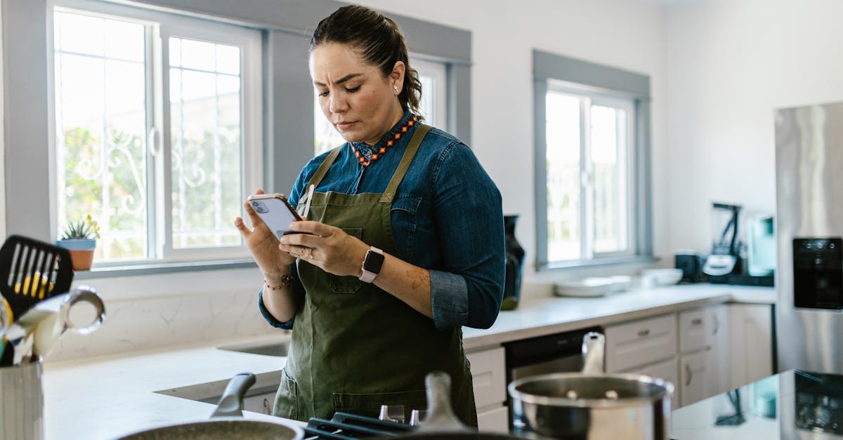 A woman in a modern kitchen following a recipe on her smartphone while cooking.