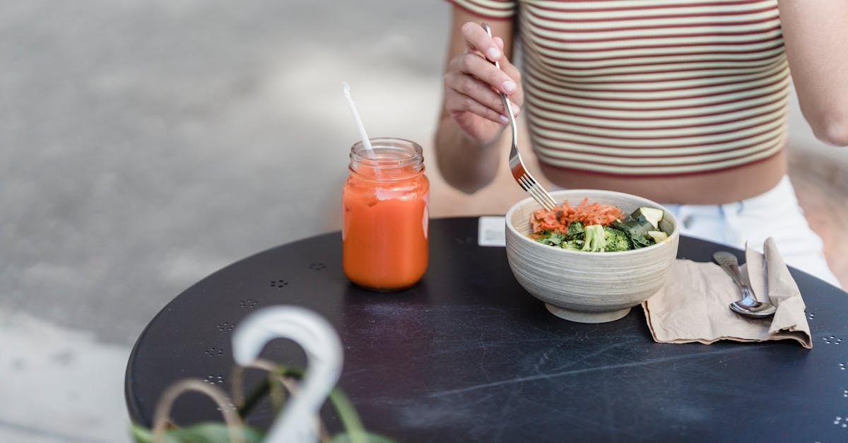 Crop unrecognizable female with bowl of delicious vegetarian salad and jar of refreshing beverage at table in urban cafe