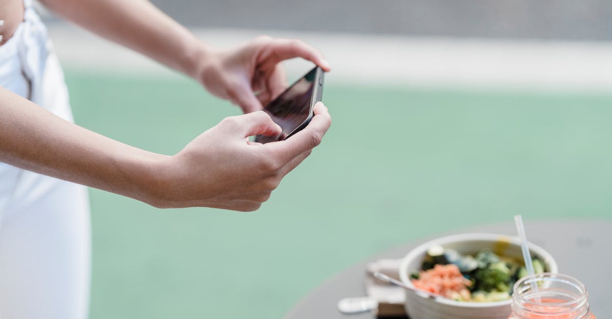 Crop unrecognizable female blogger taking photo of vegetable salad and smoothie on cellphone in street cafeteria