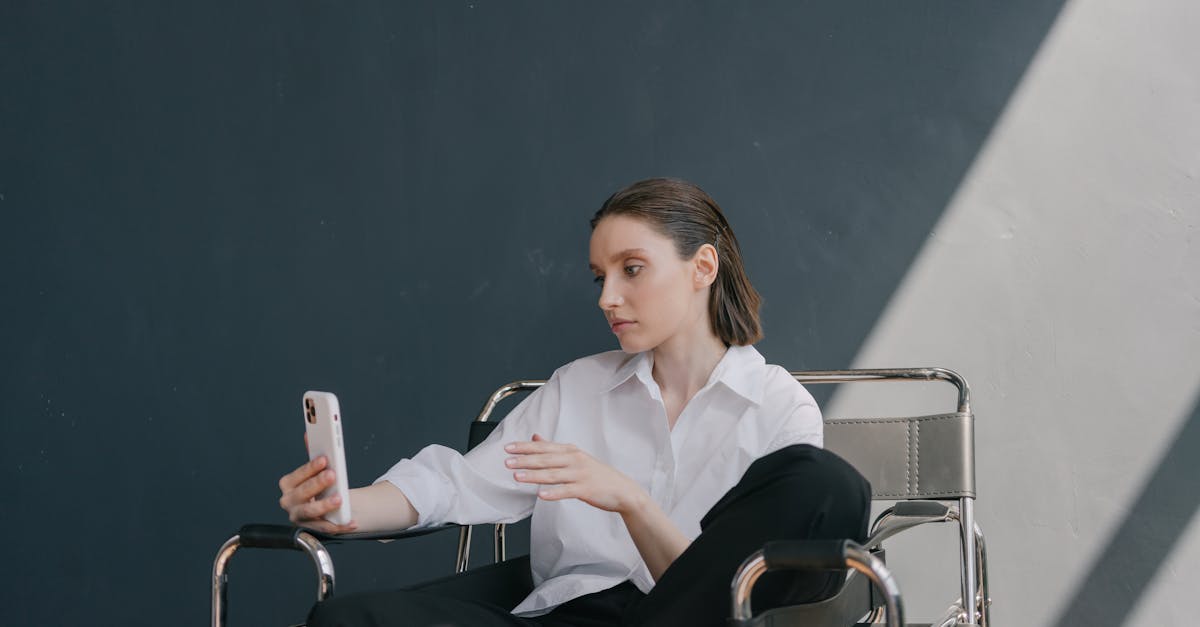 A woman sits in a modern chair using a smartphone against a gray wall.