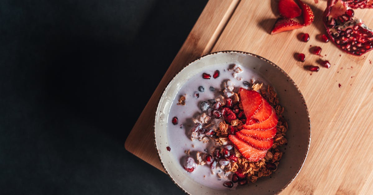 Granola bowl topped with fresh strawberries and pomegranate seeds on a wooden cutting board.