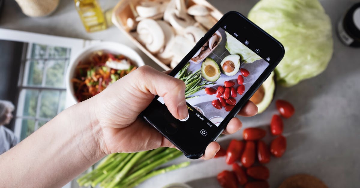 Hand holding smartphone capturing photo of fresh vegetables on a kitchen counter.
