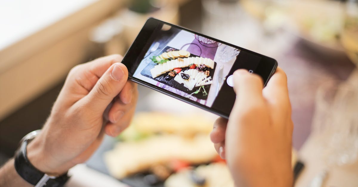 Hands holding a smartphone capturing a photo of a plated dish in a cozy setting.