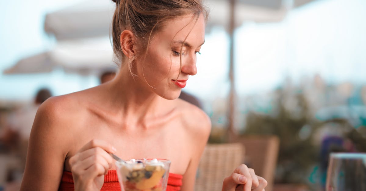 Young woman in red dress enjoying fresh fruit dessert while checking her smartphone outdoors.