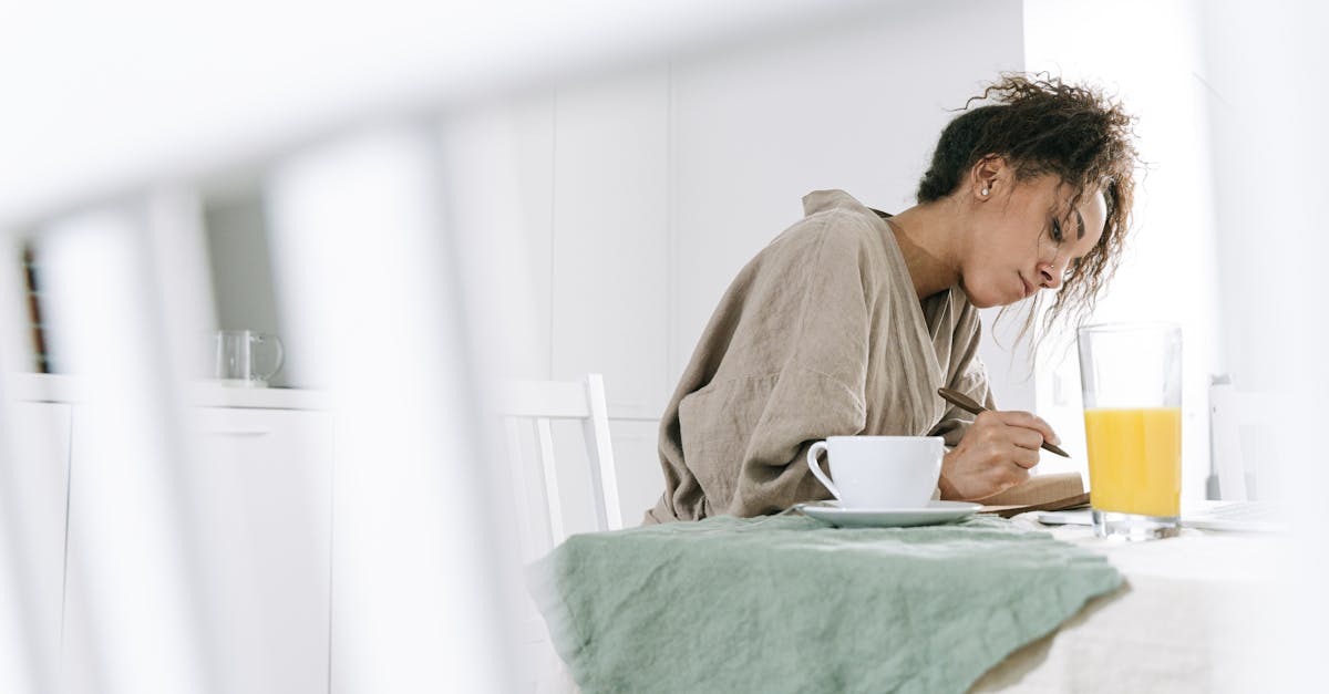 Woman in bathrobe writing in notebook, enjoying coffee and orange juice.