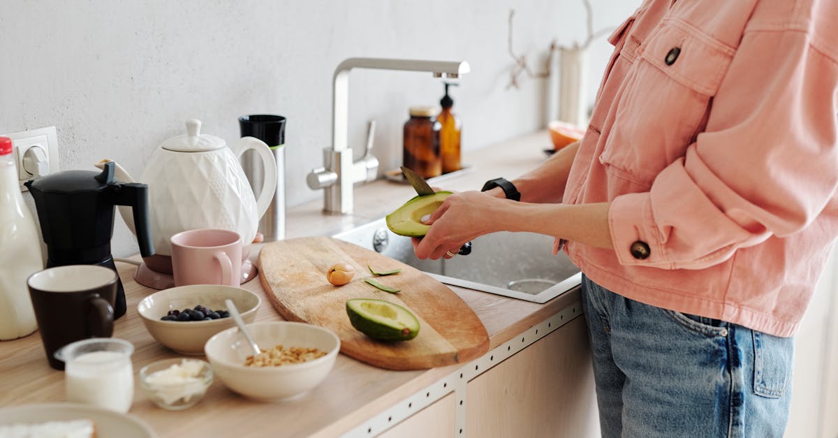 Woman in a pink shirt preparing a healthy avocado breakfast in a modern kitchen setting.
