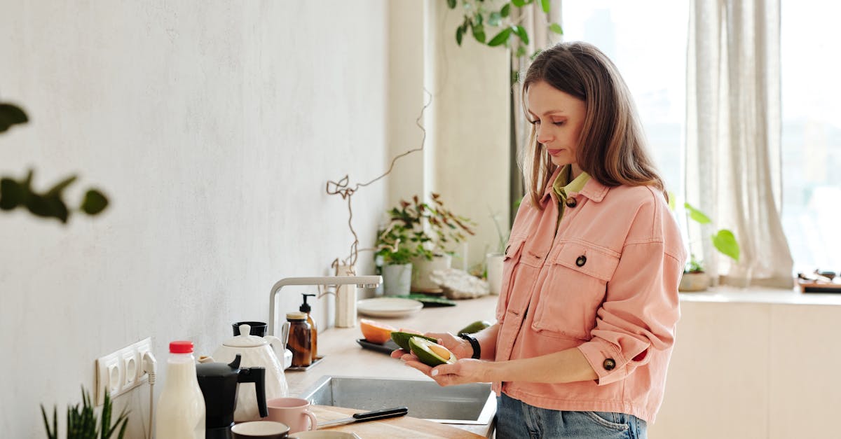 Woman preparing avocado in a modern kitchen with natural light.